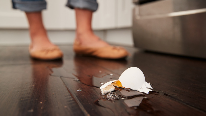 broken egg on ground with person's feet