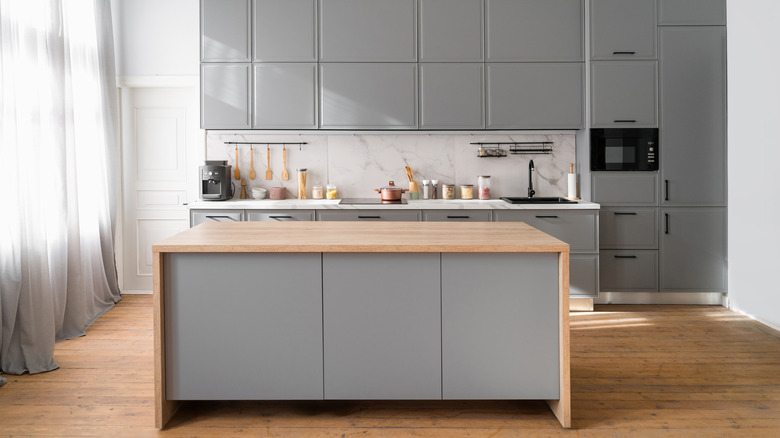 A kitchen island with a timber top and gray cabinets behind it