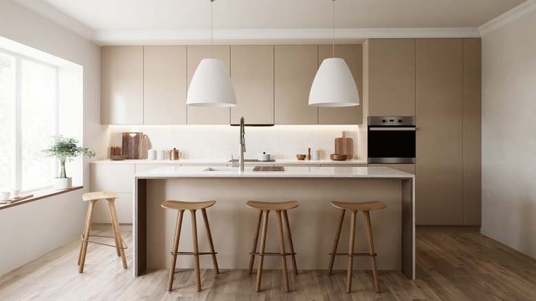 A modern minimalist kitchen with beige cabinets, white accents, and wooden stools.