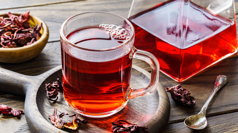 Glass cup and teapot of hot hibiscus tea on a wooden table.