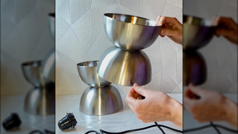 Hands send a lamp cord through a drilled hole in a metal bowl base that will become a lamp.