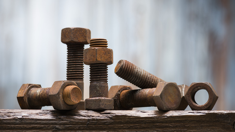 An assortment of large rusty bolts and nuts on a wooden table