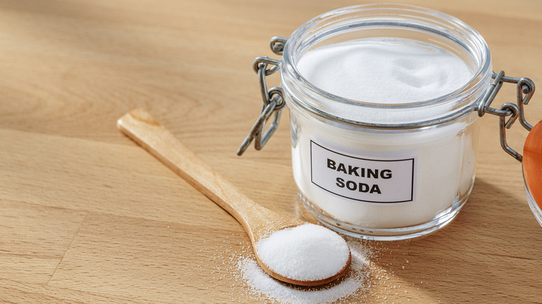 A open jar of baking soda with a wooden teaspoon next to it.