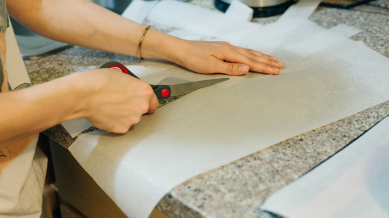 A pair of hands cut pieces of wax paper with scissors.