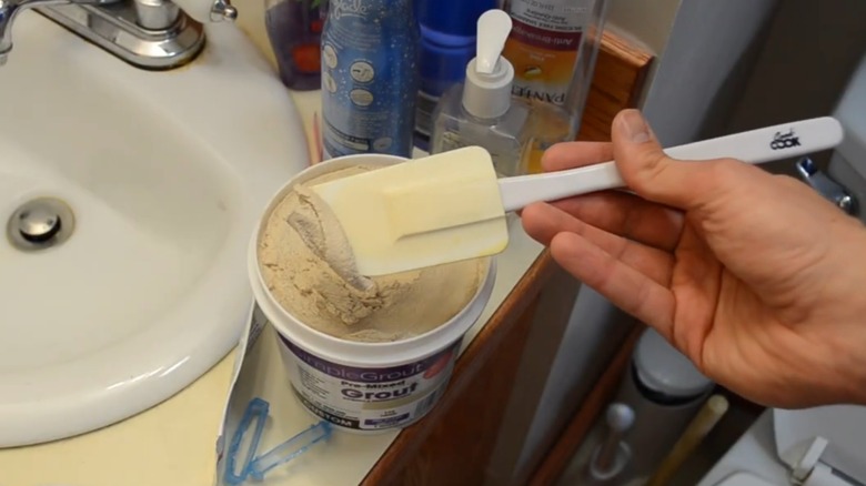 Hand scooping up grout with rubber spatula
