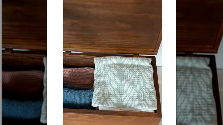 Kitchen dish towels folded up and stored in a wooden box with a lid.