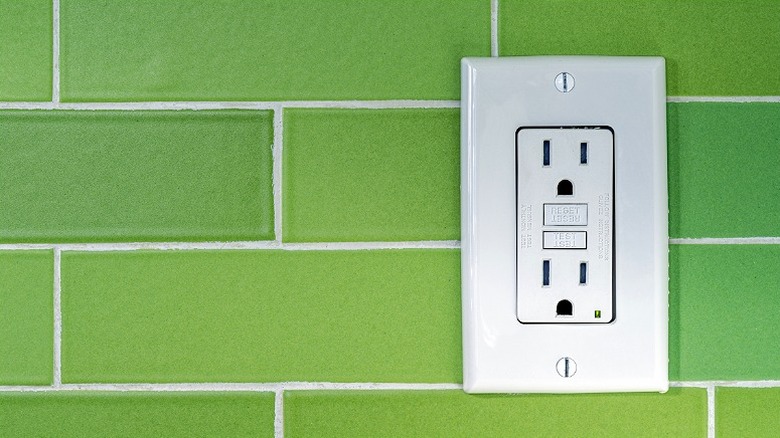 A green tiled wall with a GFCI outlet