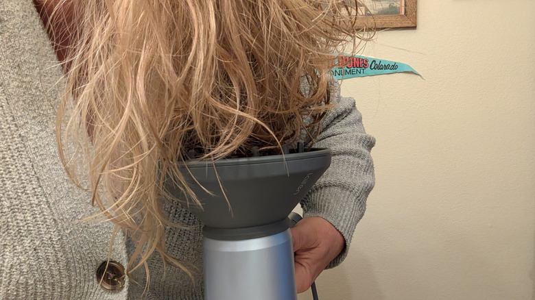 Wavy blonde hair hangs over a hair dryer diffuser.