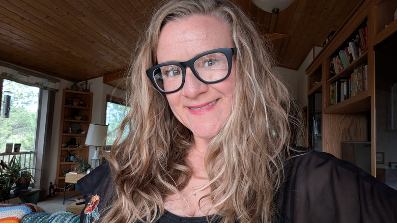 A woman with glasses and wavy blond hair is smiling.