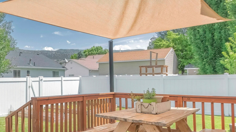 A backyard deck with a wooden table and benches covered by a large shade sail