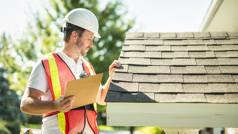 A male surveyor inspecting the shingles on a roof.