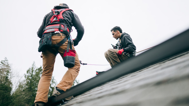 Two male roofers doing work on a slant while secured by cables.