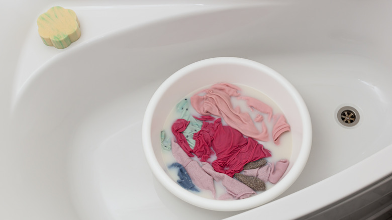 A bucket of clothes submerged in white liquid, sitting in a bathtub