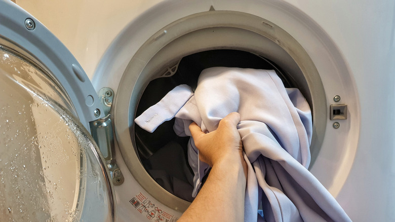 Woman's hands putting garment in the washing machine with its button open