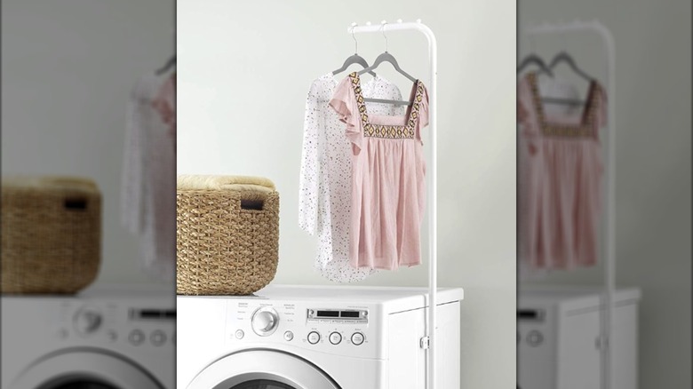 Magnetic laundry hanging rod attached to side of white washing machine with two tops hanging up on it.