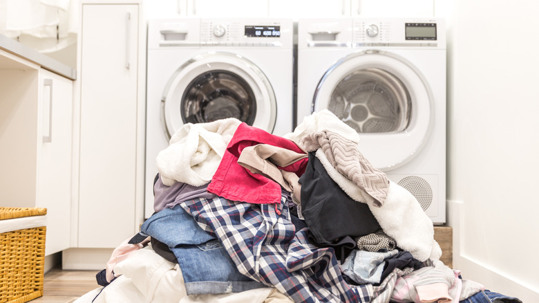 A pile of clothes on the floor in front of a washer and dryer in a small laundry room.