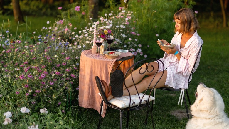 woman eating at small bistro table in garden with great pyrenees sitting nearby
