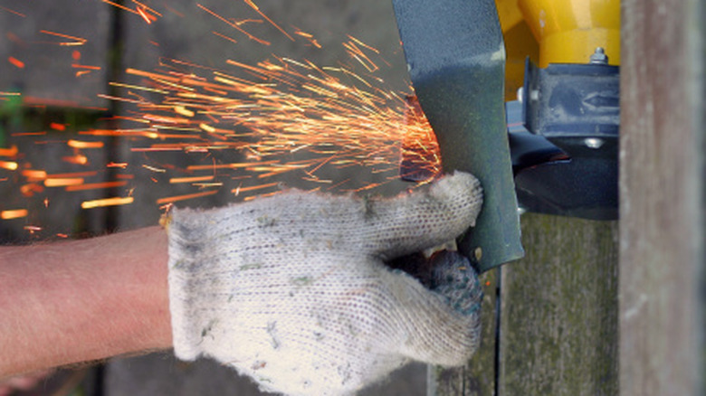 A person wearing gloves sharpening a lawn mower blade