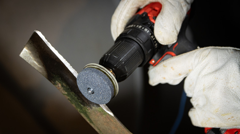 Person sharpening a mower blade with a drill attachment