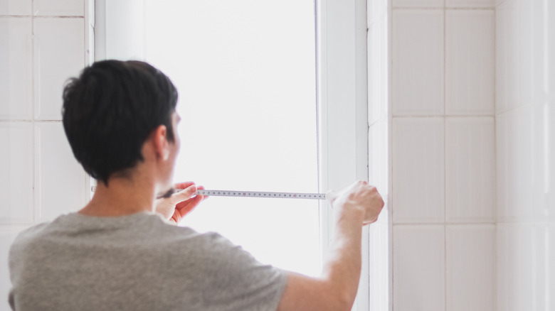 A man measures a bathroom window for treatment