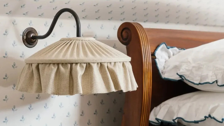 metal wall sconce with off-white fabric shade next to a bed