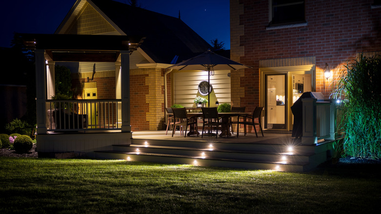 A residential backyard is illuminated in multiple places, but no one is outside using the space.