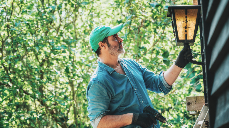 A man installs a light fixture outside of his home.