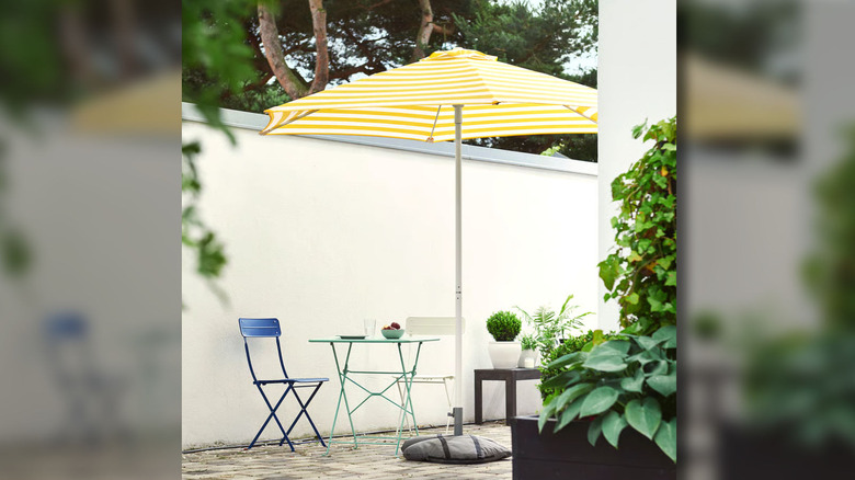 The HÖGÖN patio umbrella being used outside, shading a small patio table and chairs.