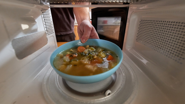 Hand putting soup in microwave