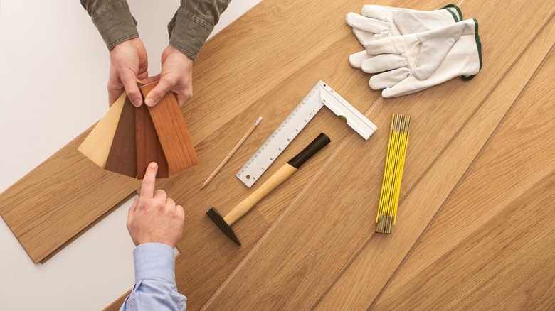 A person choosing a wood flooring option from swatches with work tools in the background