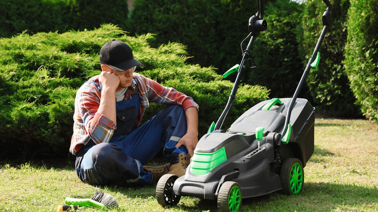 Man in hat sites with broken mower