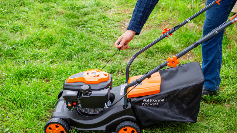 A man starts the engine of a gas lawn mower with a starter rope