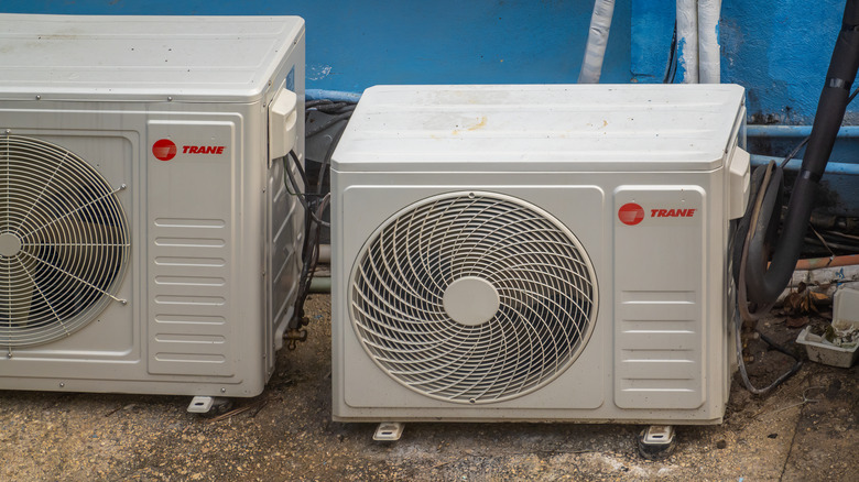 A pair of white, branded Trane air-conditioning condenser units sitting on a concrete floor.