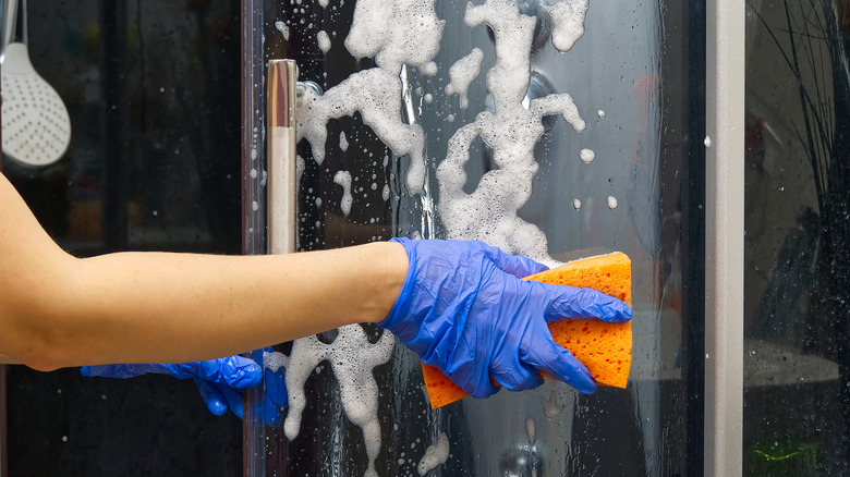Person cleaning glass shower door with orange sponge