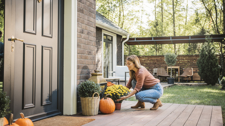 A woman decorating her front porch with flowers in decorative pots and pumpkins.