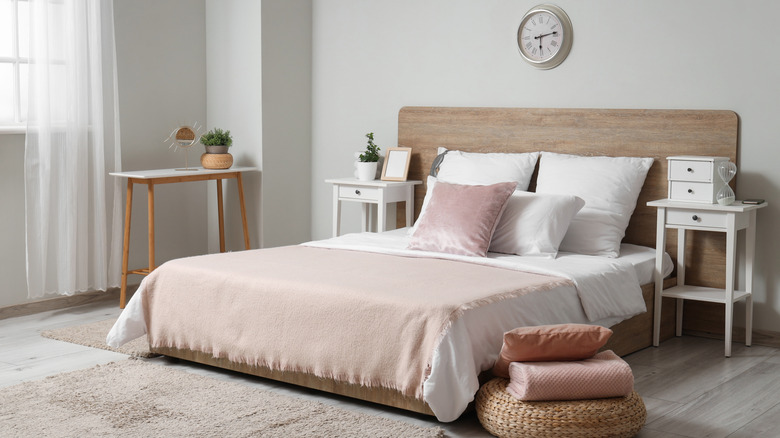 A bed styled with crisp white sheets, a pink throw blanket, and a pink statement pillow