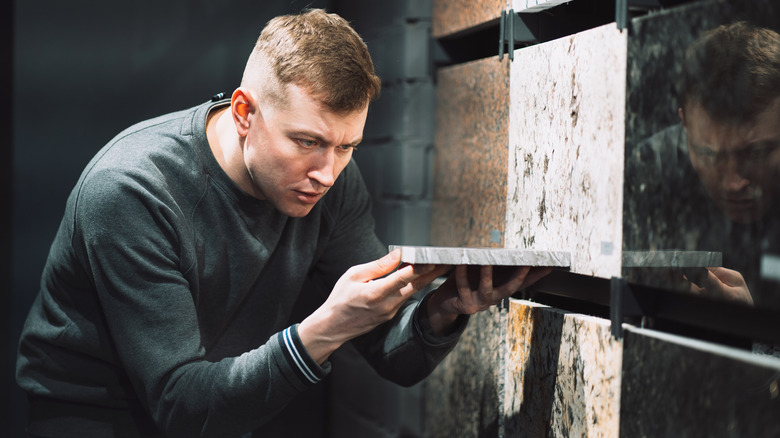 A man closely examines a tile sample, comparing it with other materials in a store