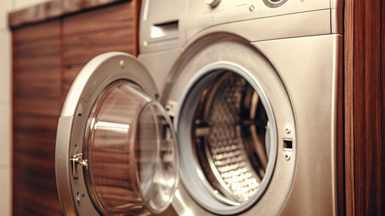 A stainless front loading washing machine with the door open surrounded by wood cabinets