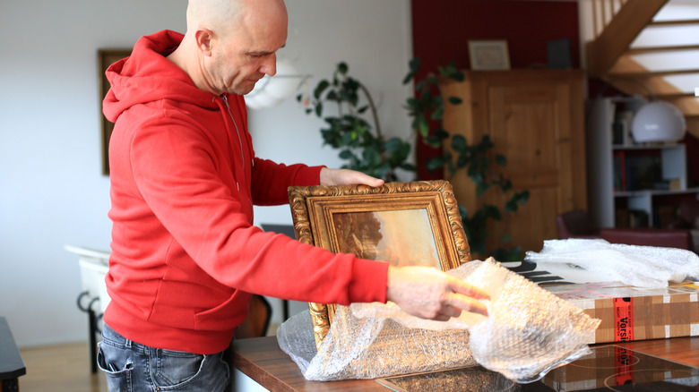 man unwrapping a framed painting on a kitchen counter
