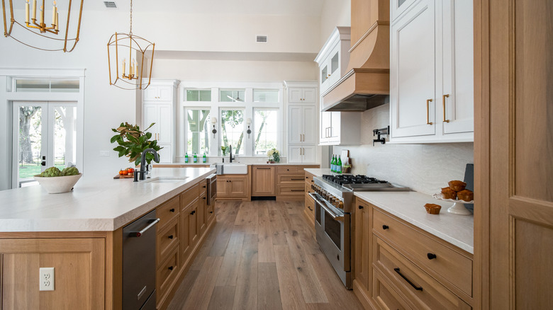 A kitchen with wood cabinetry and floors, gold light fixtures, and light filtering in the door and windows.
