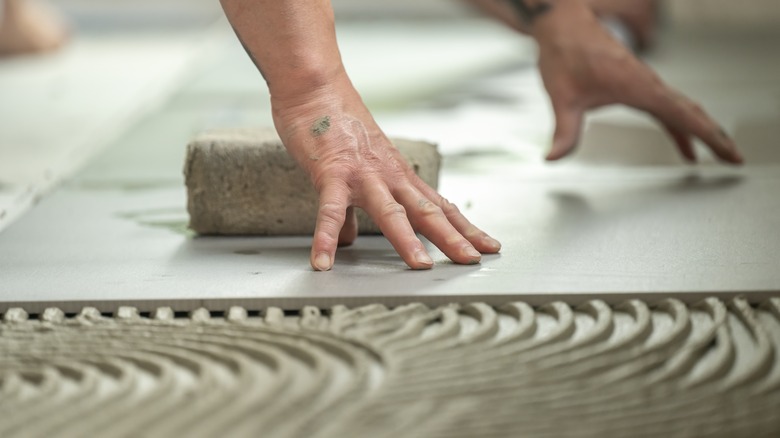 A person pressing tile into adhesive