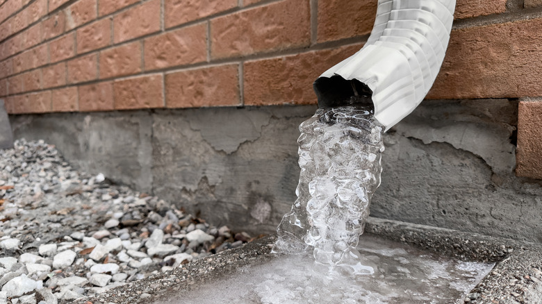Water pouring out of a downspout on the side of a brick house.