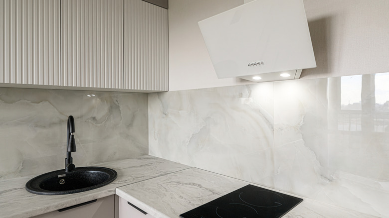 A modern kitchen featuring a black sink, white cabinets, and marble backsplash