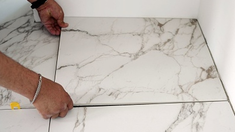 Two hands carefully placing a large marble tile on the floor