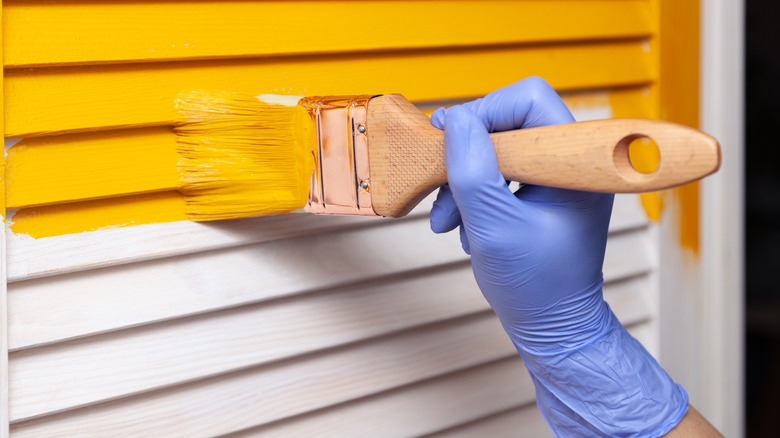 Gloved hand painting wall yellow