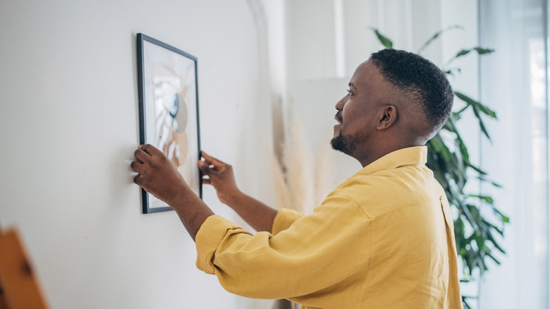 Man hanging a picture in a black frame on a wall