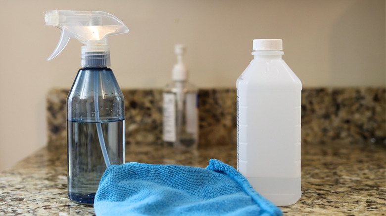 A spray bottle, cloth, and bottle of rubbing alcohol sit on a kitchen counter