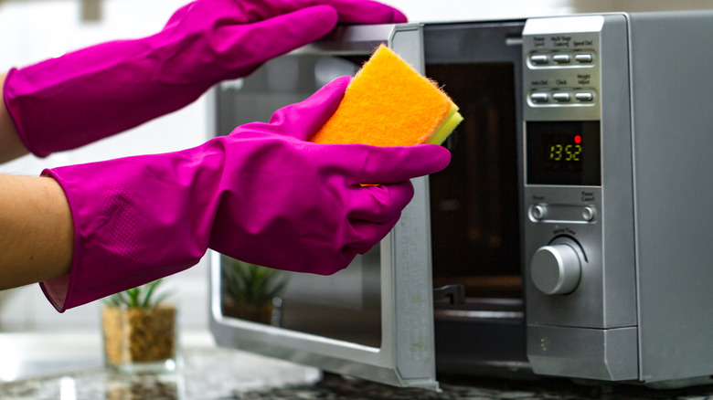 gloved hands cleaning microwave