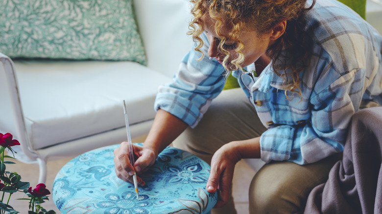 One woman painting with brush and old footstool.