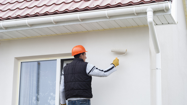 A construction worker paints the exterior of a house white with a roller
